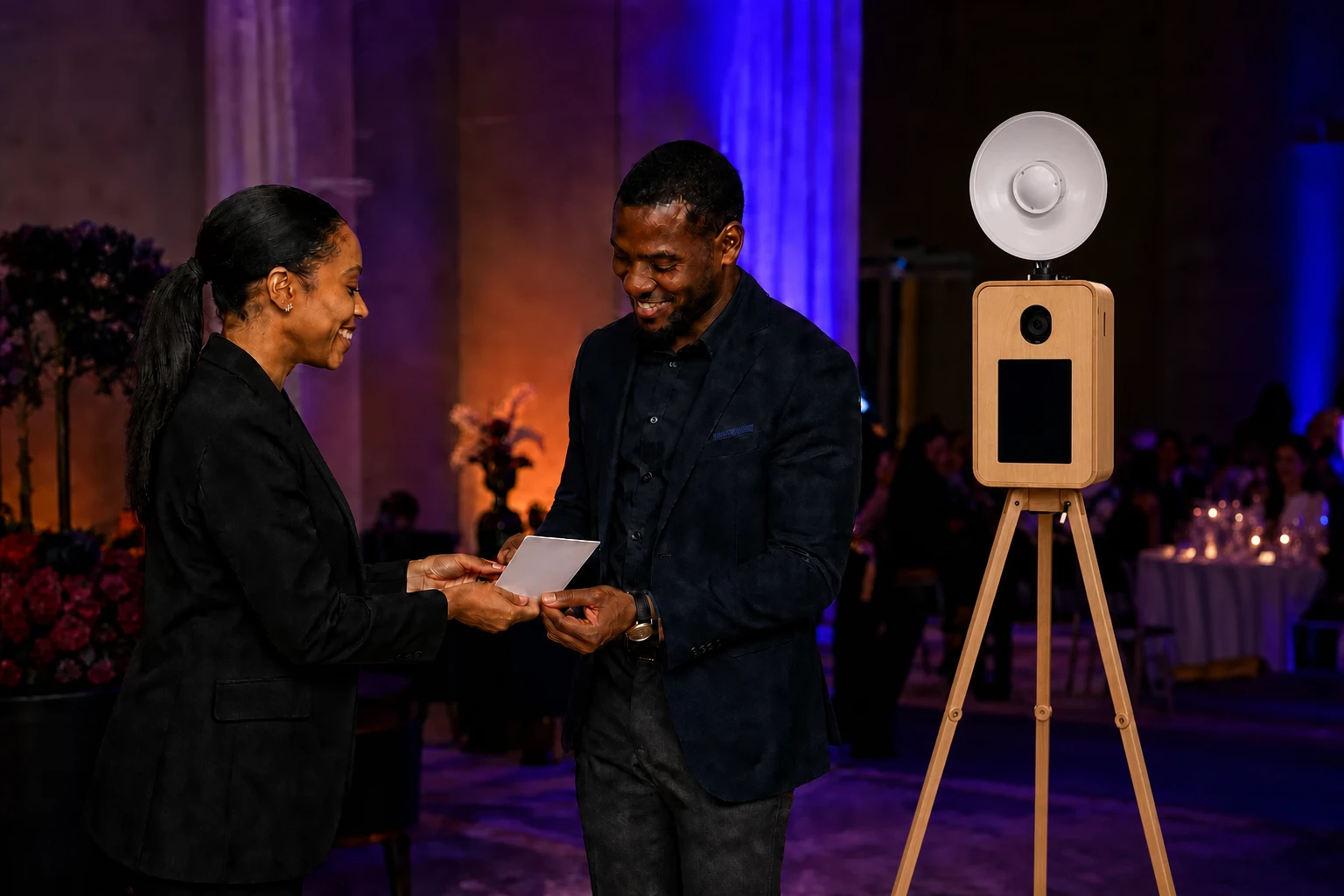 Activation host handing a portrait to a guest beside the front of the oak booth with its camera above the smaller screen